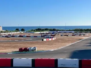 A seaside go-kart track with red-and-white barriers, curving asphalt, dry infield grass, and the Atlantic visible beyond the circuit