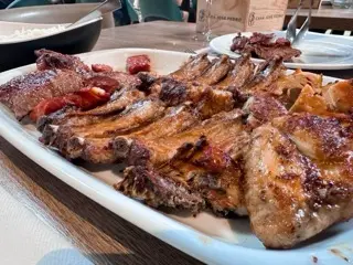 A large mixed grill platter at Central Churrasco in Matosinhos with grilled chicken, ribs, veal, chorizo, and white rice on the table