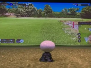 Golf ball on a tee in the foreground of an indoor simulator bay, facing a Trackman virtual green with score overlays and a hole map on screen.
