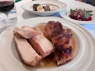 Roasted Amish chicken at Junior with sauce on the plate, side dishes in the background, and a glass of red wine on the table