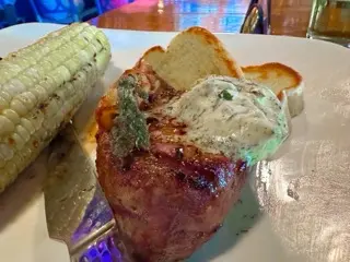 A seared filet topped with herb-flecked butter and bacon-wrapped asparagus, served with char-grilled corn and toasted bread at Moby Dicky’s
