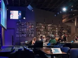The empty microphone and low stage at Zanies Nashville before the show, with reserved tables, seated guests, blue-purple lighting, and walls covered in framed comedian portraits