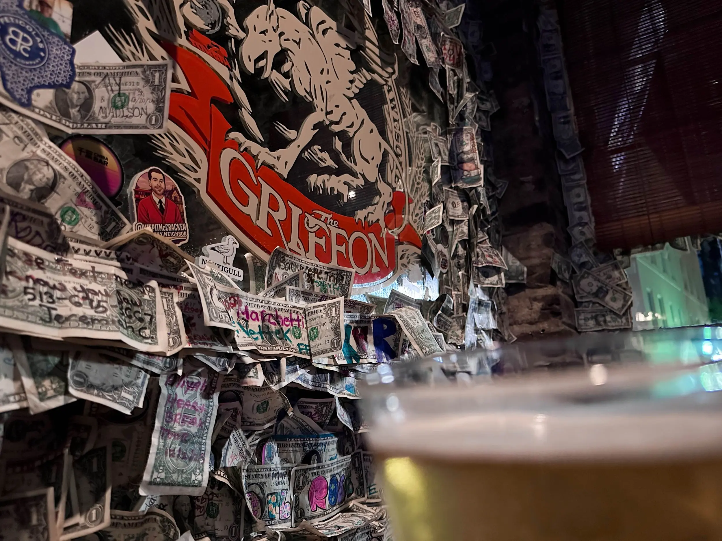 The Griffon sign surrounded by signed dollar bills on the wall, with a blurred pale beer in the foreground