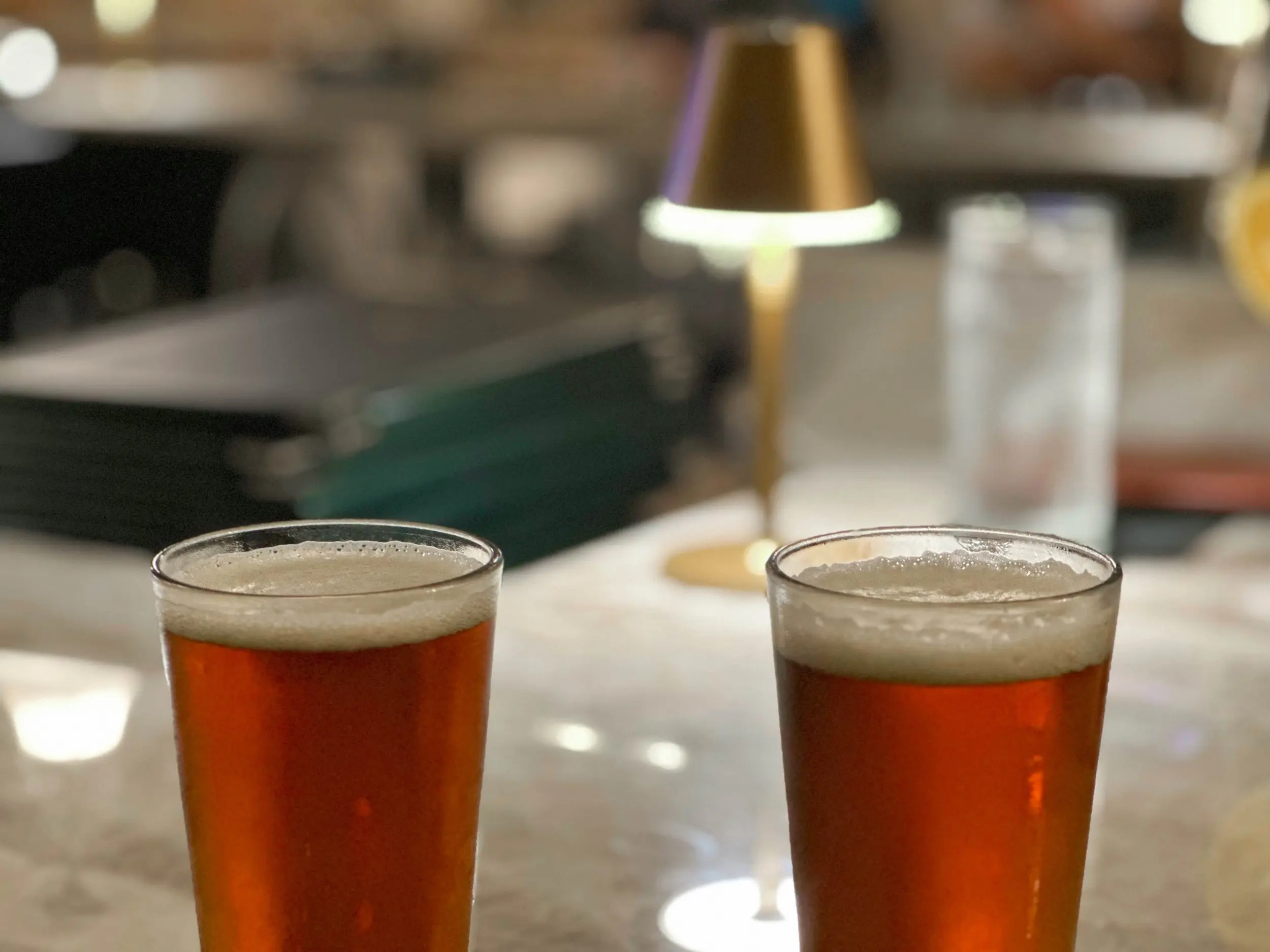 Two amber Gaelic ales with foamy heads on a polished table at Victor's, with a warm lamp and softly blurred dining room behind them