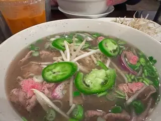 Bowl of rare steak pho with jalapeños, bean sprouts, and herbs beside a red Thai tea